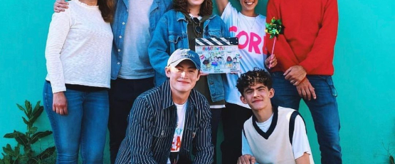 The cast of Heartstopper poses for a photo in front of a bright blue wall. 