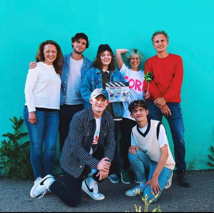 The cast of Heartstopper poses for a photo in front of a bright blue wall. 